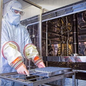 Symbiosis scientist wearing full PPE equipment loading vials into lyophiliser