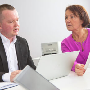 Alison listening to John, both sat at a desk in the Symbiosis Pharmaceutical offices