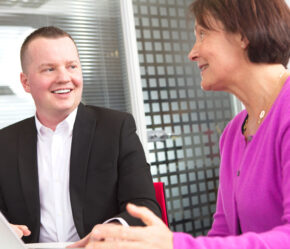 John smiling at Alison as they both sit at a desk in Symbiosis Pharmaceutical offices