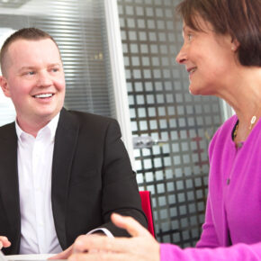 John smiling at Alison as they both sit at a desk in Symbiosis Pharmaceutical offices