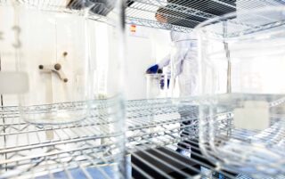 Close up image looking through wire shelving, past beakers and into a gmp biologics manufacturing labratory