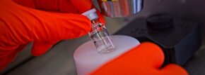 Gloved hands of a biologics CMO scientist removing a vial from the automatic crimper