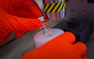 Gloved hands of a biologics CMO scientist removing a vial from the automatic crimper