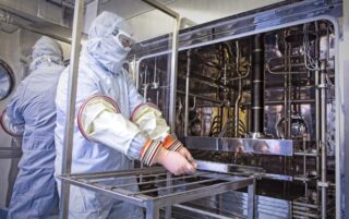 Symbiosis scientist wearing full PPE loading a tray of vials into the lyophiliser