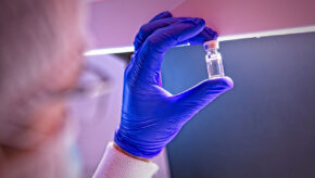 Gmp biologics manufacturing scientist holding a vial of drug product up to the light for visual inspection