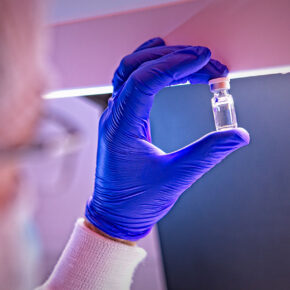 Gmp biologics manufacturing scientist holding a vial of drug product up to the light for visual inspection