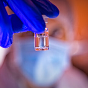 Gmp biologics manufacturing technician wearing PPE holding up to the camera a vial of drug product.