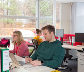 Male and female aseptic manufacturing scientists sat at a long desk of computers in the Symbiosis Pharmaceutical Services office.