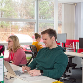 Male and female aseptic manufacturing scientists sat at a long desk of computers in the Symbiosis Pharmaceutical Services office.