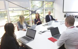 Members of the Symbiosis leadership team sat around a board room table speaking with their laptops on front of them and a large window to the rear of the room.